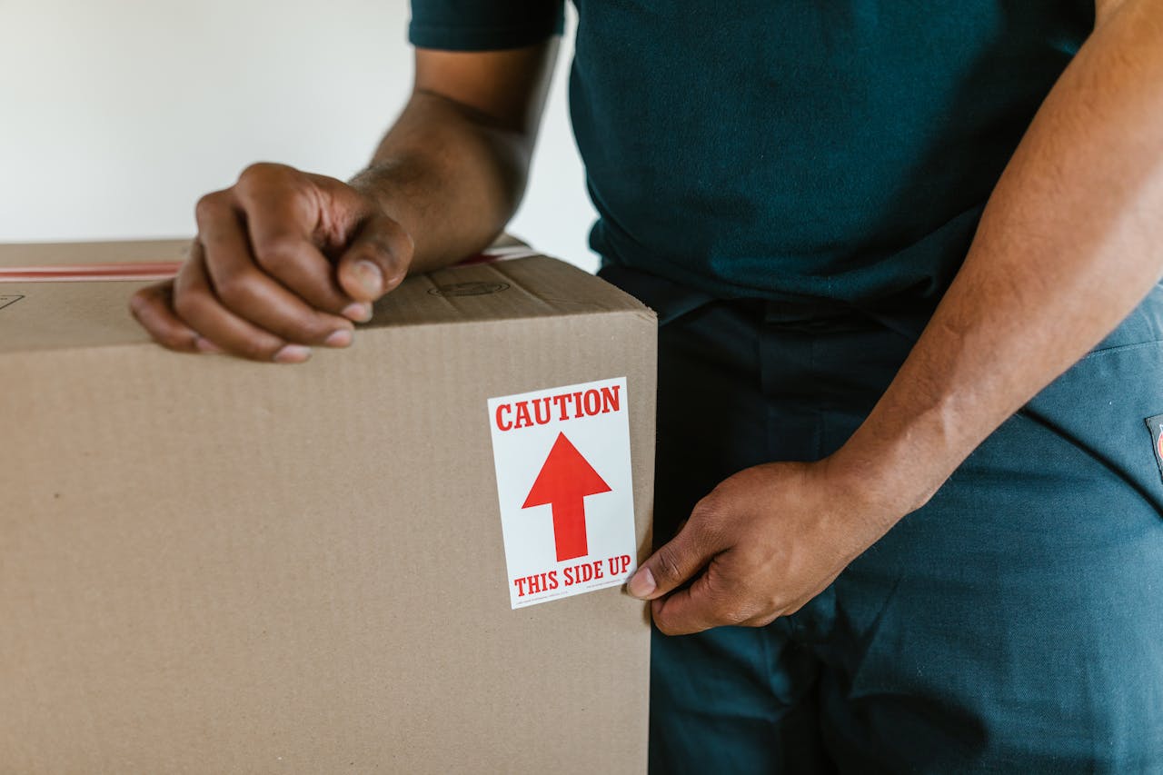 A person handling a moving box with a 'caution this side up' label indoors.